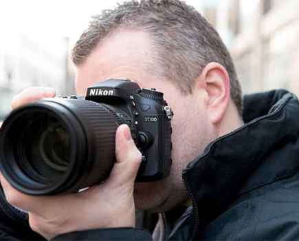 Man holding a black Nikon D7 camera to his eye