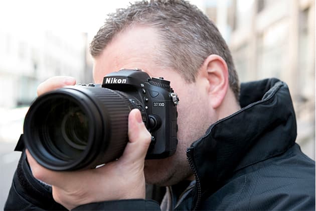 Man holding a black Nikon D7 camera to his eye