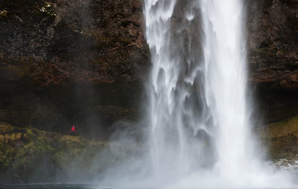 Man in red jacket standing next to tall waterfall. Photo: Jeremy Walker