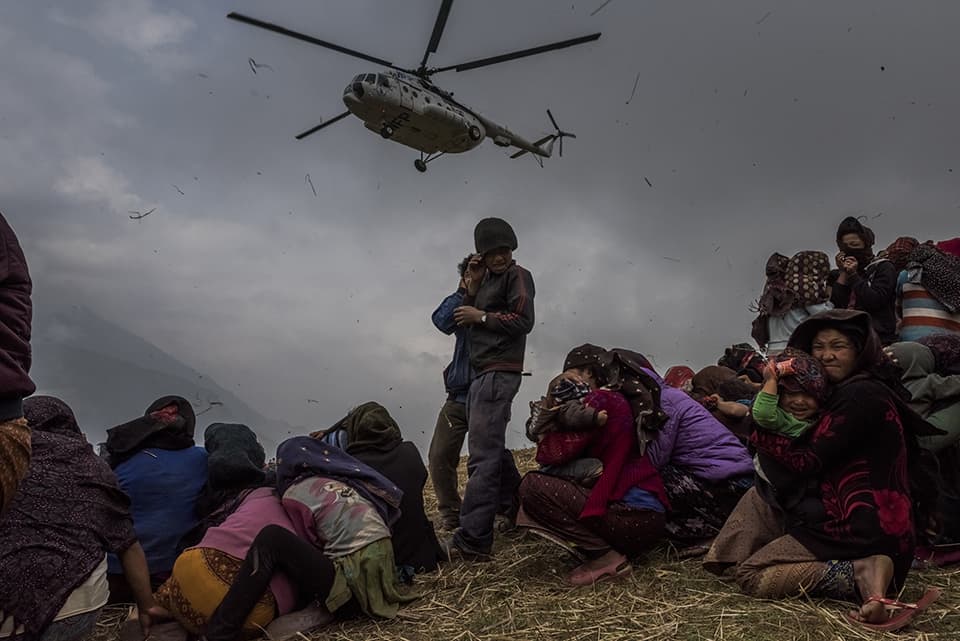 3—Gumda, Nepal. Saturday, May 09, 2015: Nepalese villagers look on as they watch a helicopter picking up a medical team, dropping aid at the edge of a makeshift landing zone on May 9, 2015 in the village of Gumda, Nepal. On the 25th of April, just before noon local time, as farmers were out in fields and people at home or work, a devastating earthquake struck Nepal, killing over 8,000 people and injuring more than 21,000 according to the United Nations Office for the Coordination of Humanitarian Affairs. Homes, buildings and temples in Kathmandu were destroyed in the 7.8 magnitude quake, which left over 2.8 million people homeless, but it was the mountainous districts away from the capital that were the hardest hit. Villagers pulled the bodies of their loved ones from the rubble by hand and the wails of grieving families echoed through the mountains, as mothers were left to bury their own children. Over the following weeks and months, villagers picked through ruins desperate to recover whatever personal possessions they could find and salvage any building materials that could be reused. Despite relief teams arriving from all over the world in the days after the quake hit, thousands of residents living in remote hillside villages were left to fend for themselves, as rescuers struggled to reach all those affected. Multiple aftershocks, widespread damage and fear kept tourists away from the country known for its searing Himalayan peaks, damaging a vital climbing and trekking industry and compounding the recovery effort in the face of a disaster from which the people of Nepal continue to battle to recover.