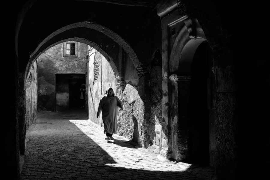Black and white capture of a monk walking through monestary corridor