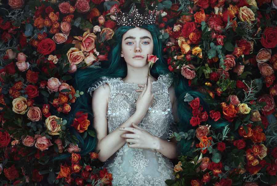 Woman with green hair and a crown lying in a bed of rose from an aerial view