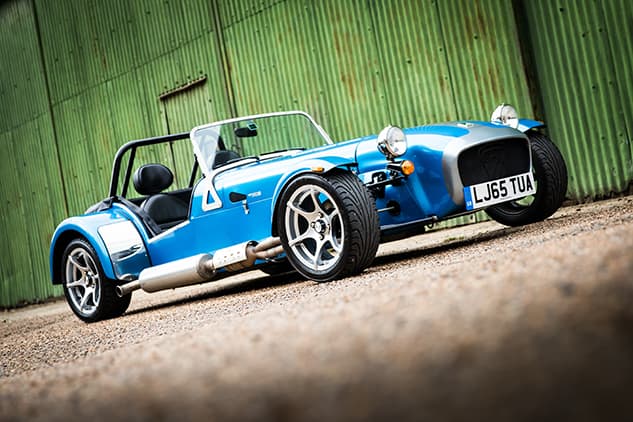 blue Caterham sports car side view in front of a green farm building