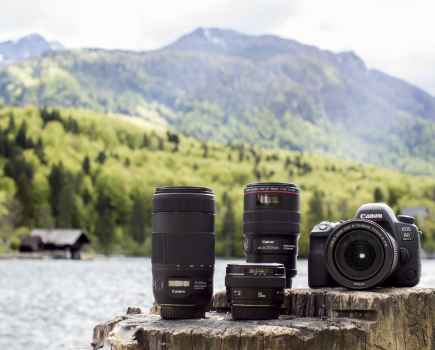 Canon EOS 6D Mark II Camera and attachments sat on a log with a lake behind