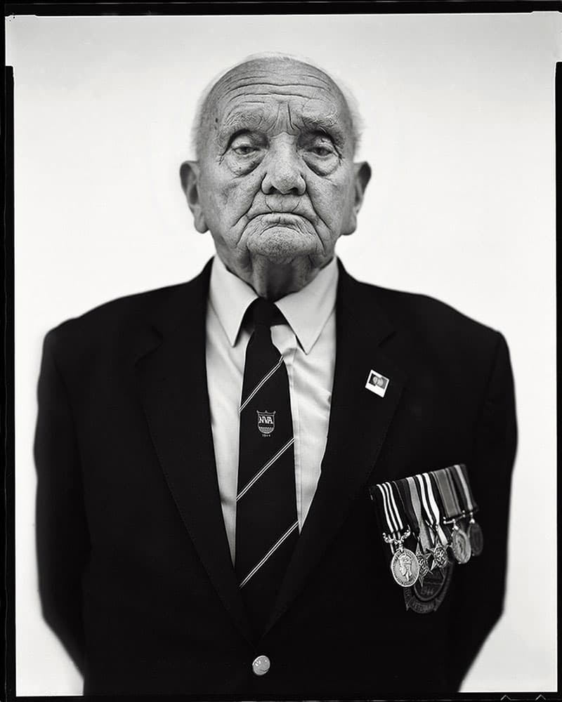 Yerbury. Black and white shallow depth of field portrait of an elderly man in suit and war medals against a plain white background.