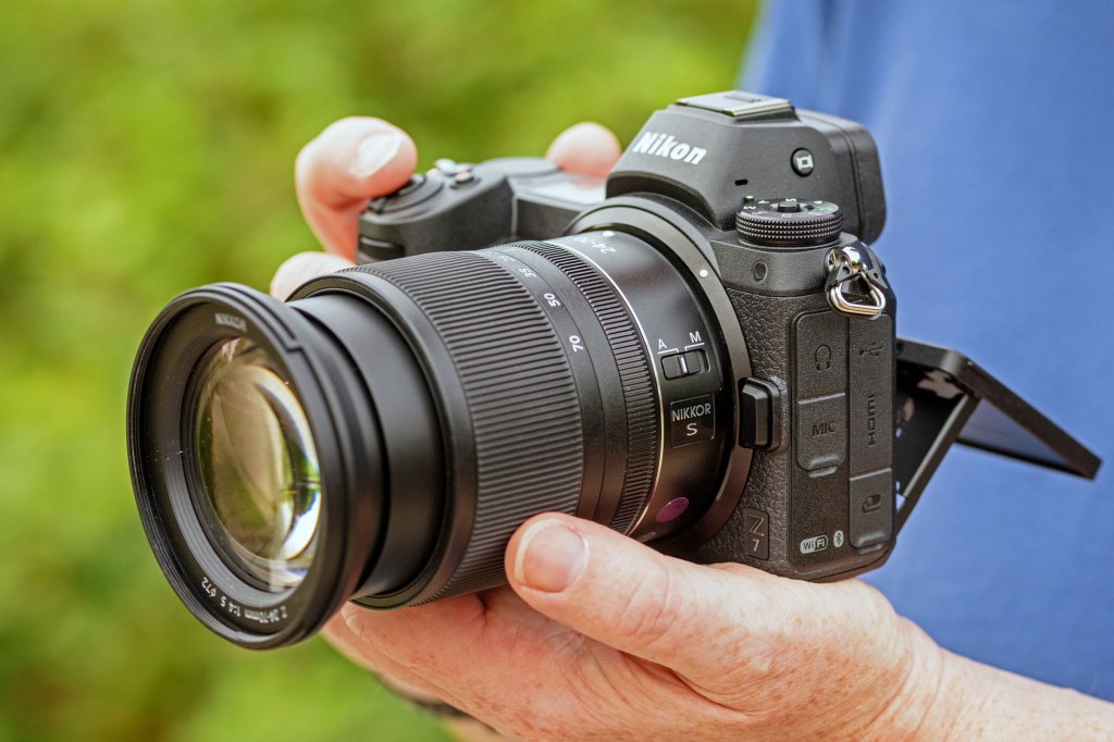 Hand holding the black Nikon Z7 camera, with the LCD screen tilted down