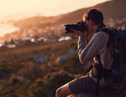 Photographer with a backpack holding a camera to their face and capturing the view in golden sunlight