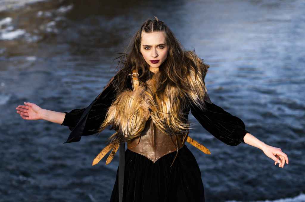 portrait of a woman wearing a feather harness stood in front of water