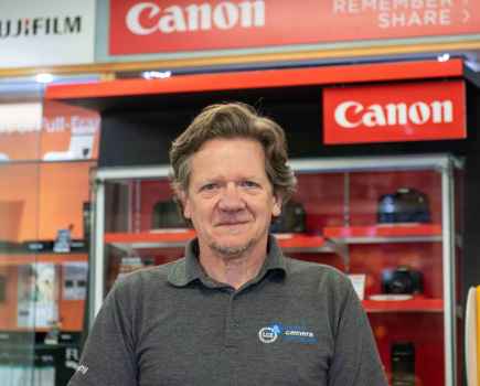 Headshot of a man in a grey top stood in front of a red Canon sales cabinet