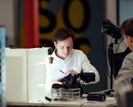 Man in white shirt sat at a desk admiring a camera in a photography studio