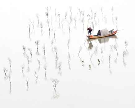 High up, distanced shot of a man in a yellow boat on still water