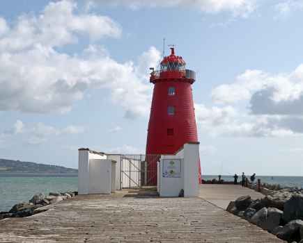 Poolbeg red lighthouse at the end of a stone path with a coastal backdrop