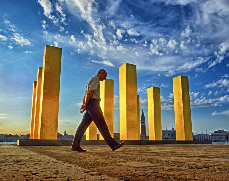 Man walking past 6 large yellow columns with bright blue skies above