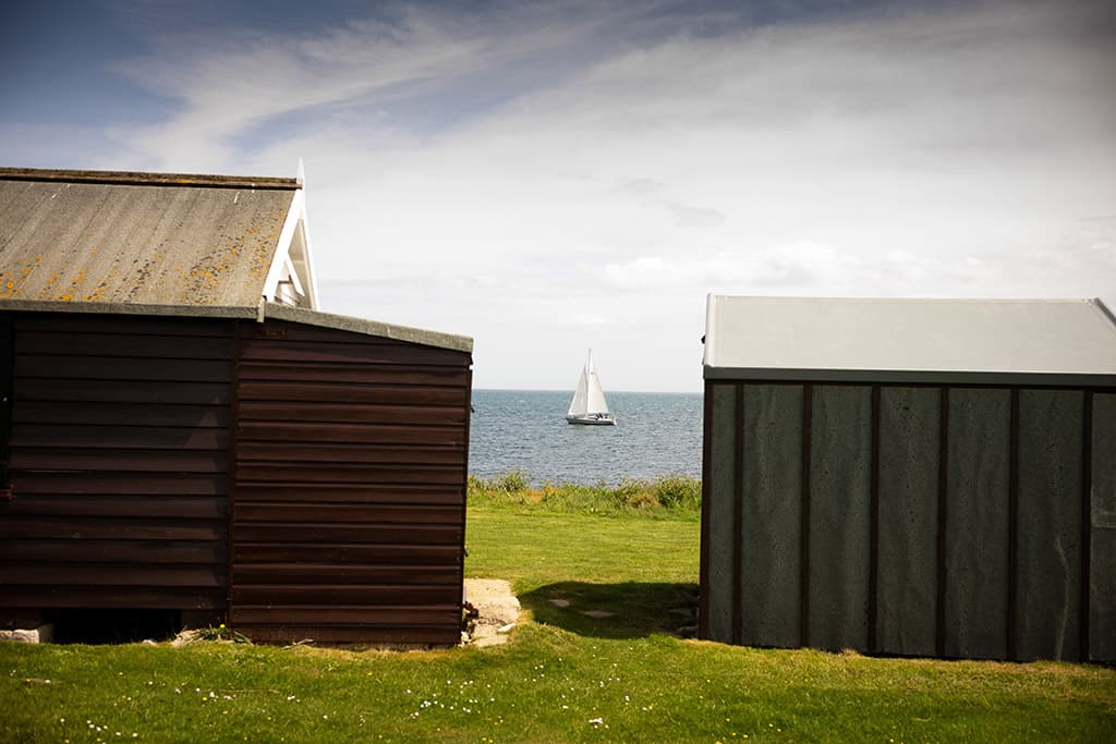 View of a sailboat in the water between two beach huts in Portland