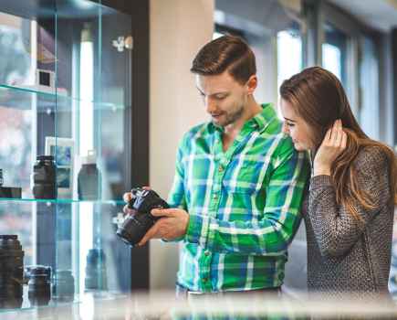 A man in a green check shirt and a woman in grey admiring a camera in a photography store