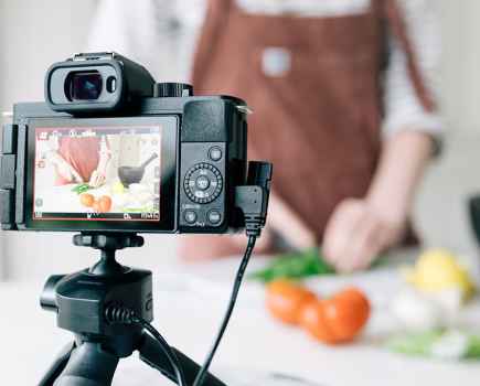 Panasonic Lumix G100 on a tripod filming someone cooking behind