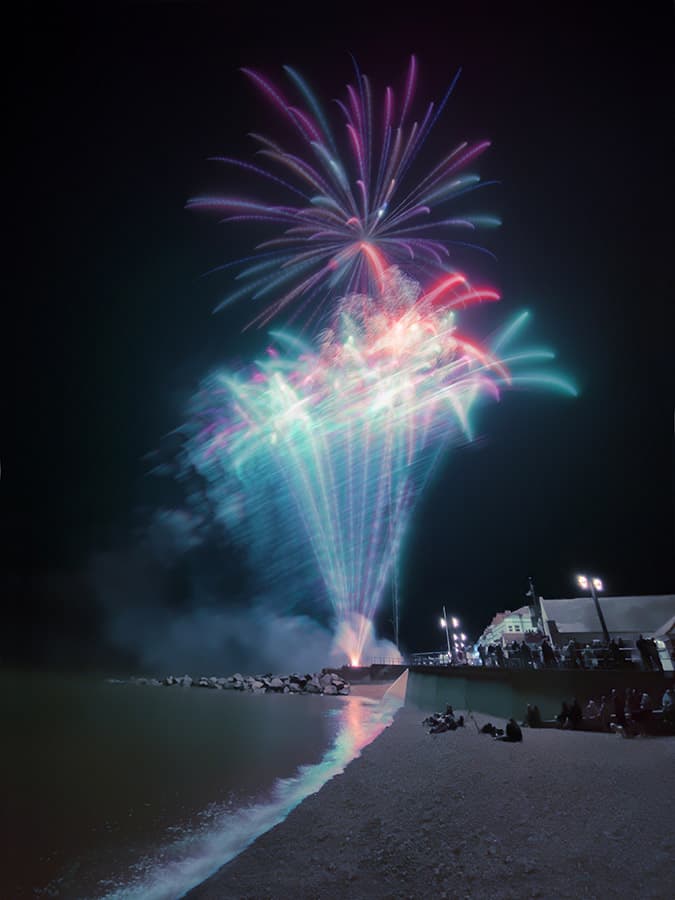 night scene on the beach overlooking a pink and blue firework display