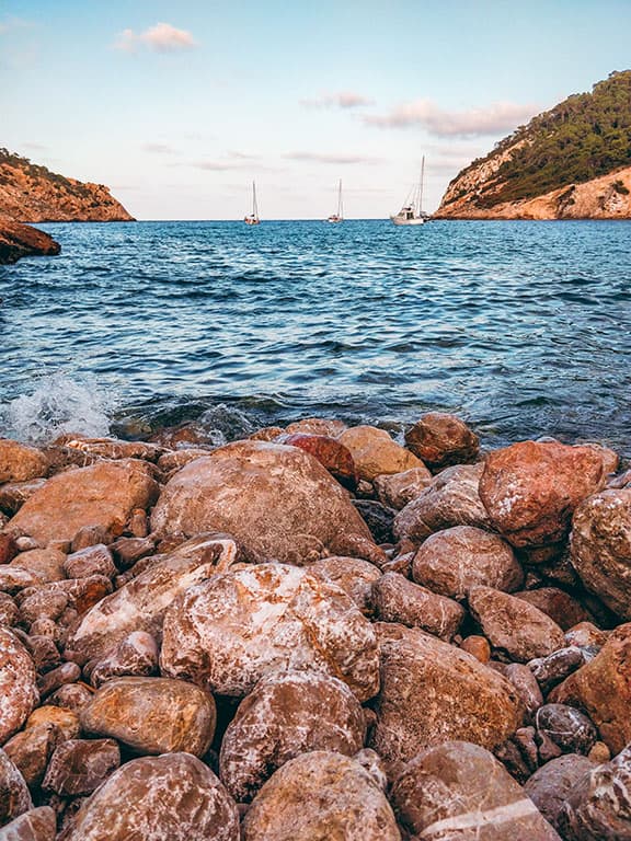 rocky landscape over looking a bay in Ibiza with sailing boats. smartphone photos 