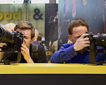 Two men behind a table testing Nikon cameras