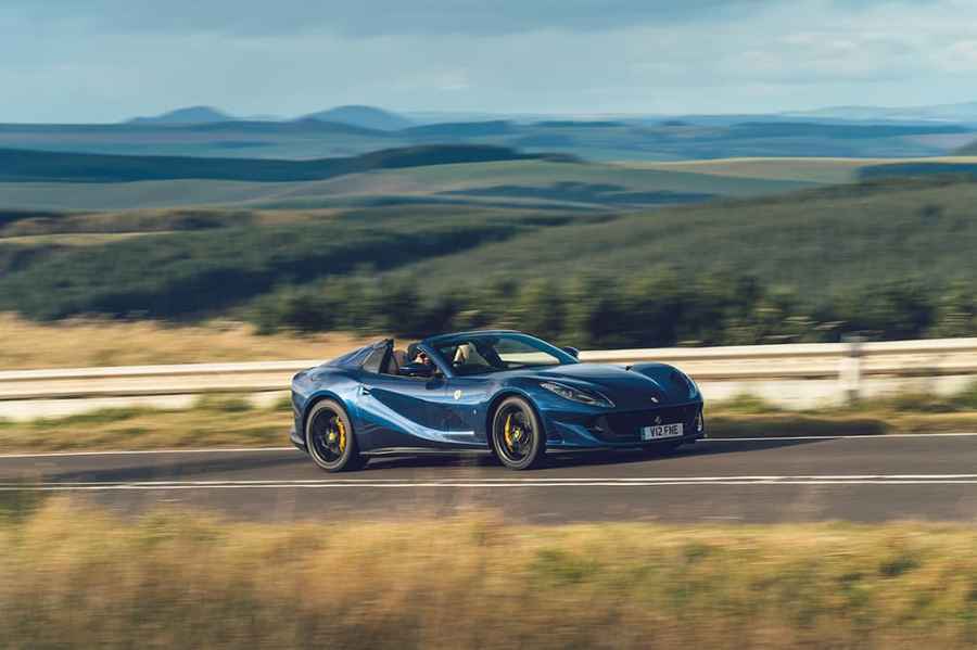 A blue Ferrari 812 GTS driving on a tarmac road in the countryside