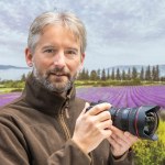 headshot of Guy Edwardes with his camera, purple fields of lavender and a line of trees in the background