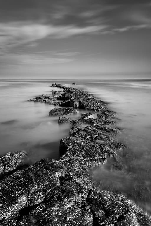 black and white long exposure landscape of a line of rocks in the sea