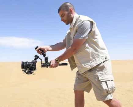 A man dressed in all beige filming with a camera in the desert
