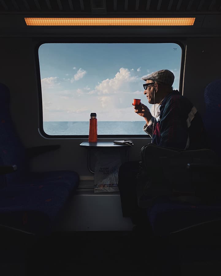 man drinking tea from a flask on the train looking out the window smartphones for street photography