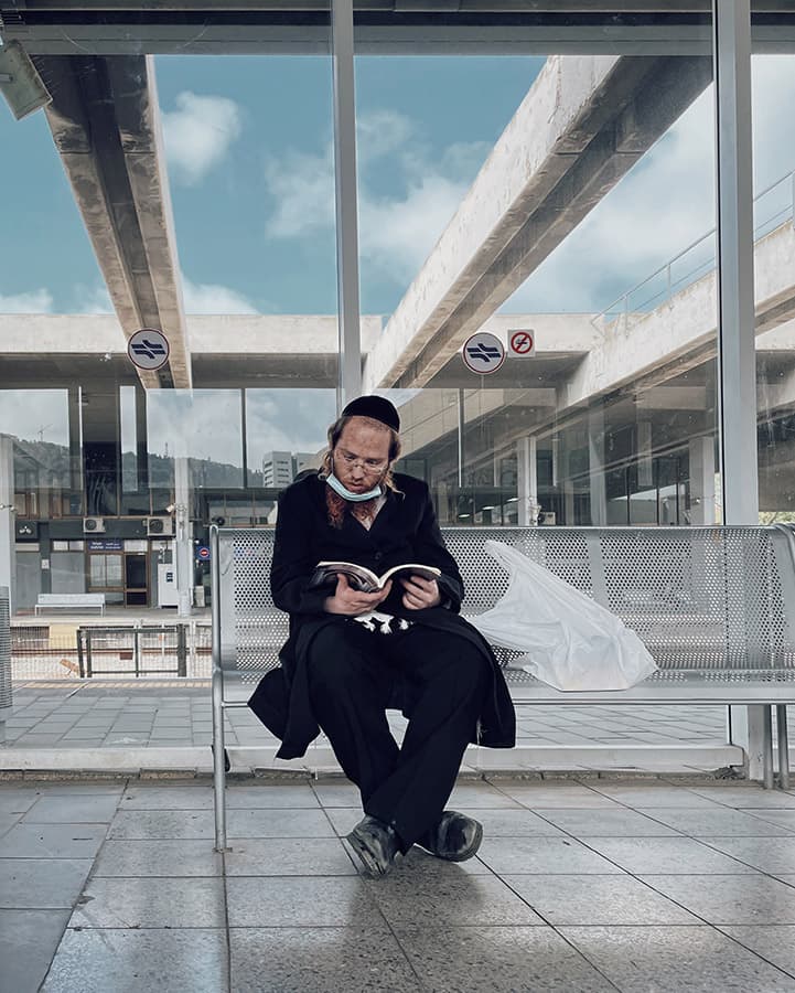 person waiting at a station sat on a bench reading smartphone street photography
