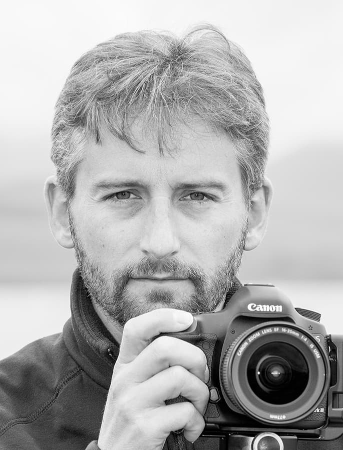Grey headhshot of a man holding a Canon camera