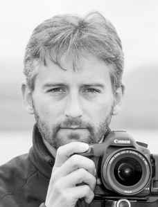 Grey headhshot of a man holding a Canon camera
