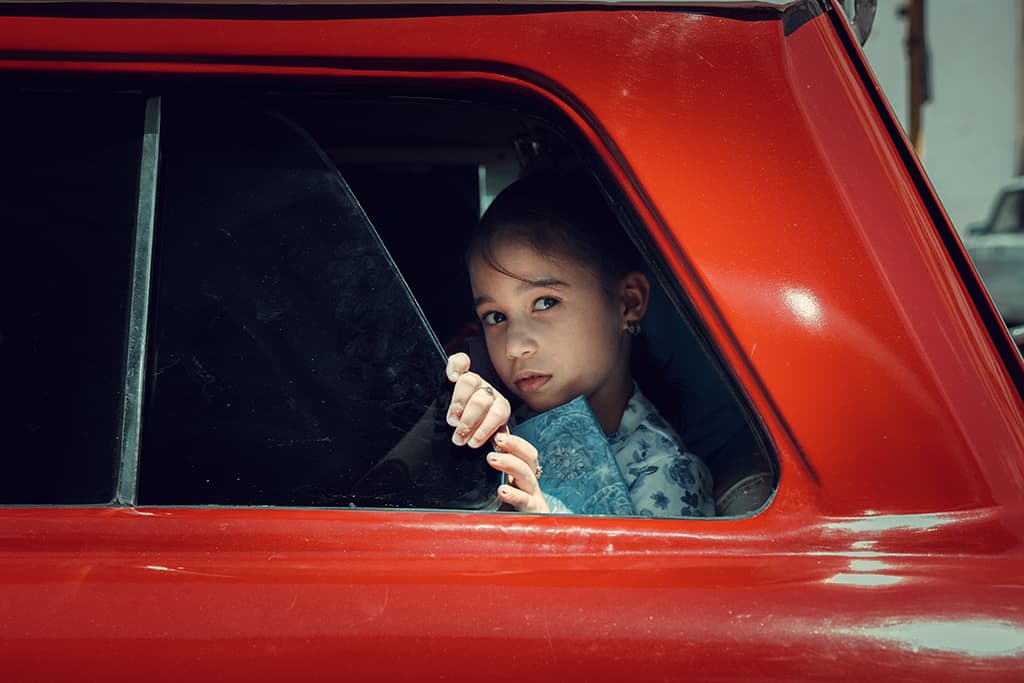 Image of a young girl looking out a bright red car
