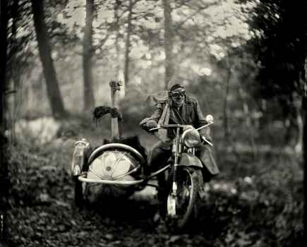 Sepia tone shot of a man on a bike with a sidecar in the woods