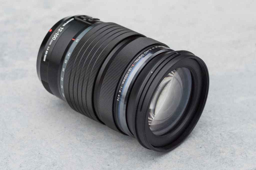 Olympus M.Zuiko Digital ED 12-100mm f/4 IS Pro lens photographed against a grey textured surface
