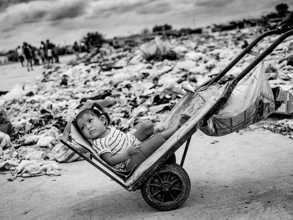  young girl being transported home by her dad along the garbage site, on the abandoned airstrip outside Maicao in Colombia. More than 8.5 million people in Colombia urgently need help. The financial collapse in Venezuela has left many with no access to emergency aid, shelter, clean drinking water or food. Children pay the highest price. © Jan Grarup, Denmark, Finalist, Professional, Documentary Projects, 2022 Sony World Photography Awards 
