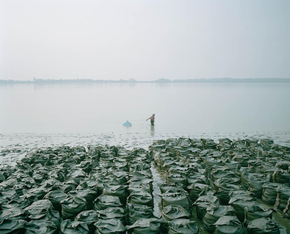 A woman walking in the water, and catching small fish or shrimps near sandbags soaked in the river, Gabura Union, Bangladesh. © Shunta Kimura, Japan, Finalist, Professional, Environment, 2022 Sony World Photography Awards