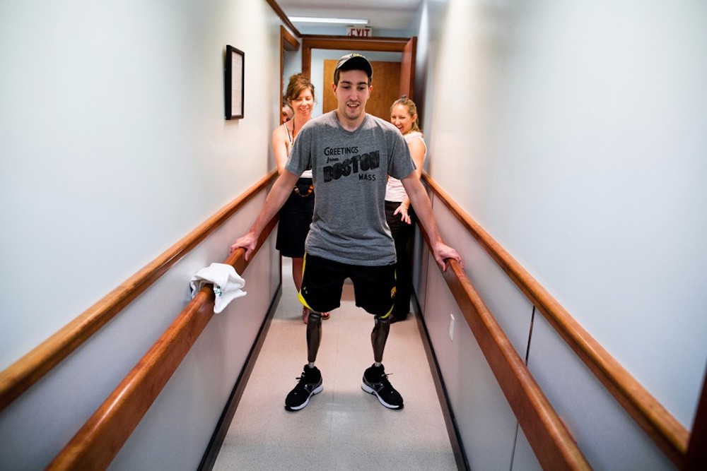 At a final fitting for his prosthetic legs, Jeff Bauman walked on his own for the first time since the day of the marathon. His girlfriend Erin, looked at him and said, 'I love that you're standing right now,' before coming around to steady him and kiss him. Josh Haner won a Pulitzer Prize in 2014 for his coverage of Boston Marathon bomb victim Jeff Bauman. Image: Josh Haner/The New York Times