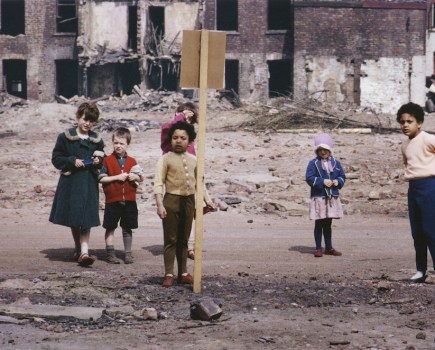 Street Scene, Hulme, Manchester. A group of children standing by a sign in front of a 'cleared' row of houses, the shells of houses due for demolition behind, 1965. Image: Shirley Baker Photography © Nan Levy for the Esta