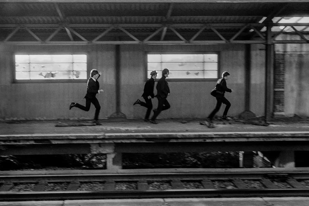 The Beatles during filming of A Hard Day's Night. The Beatles film was primarily shot on a moving train. The four Beatles running on train platform, London, England, 1964. © David Hurn/Magnum Photos