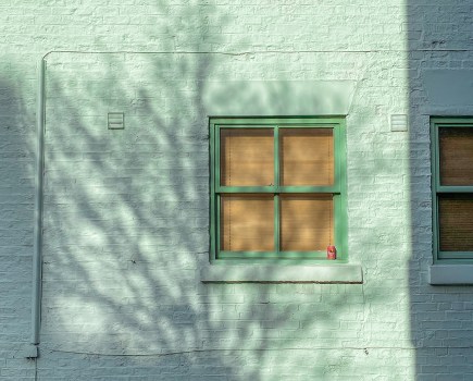 Pale grey painted brick building with a brighter green square window frame, in Leeds