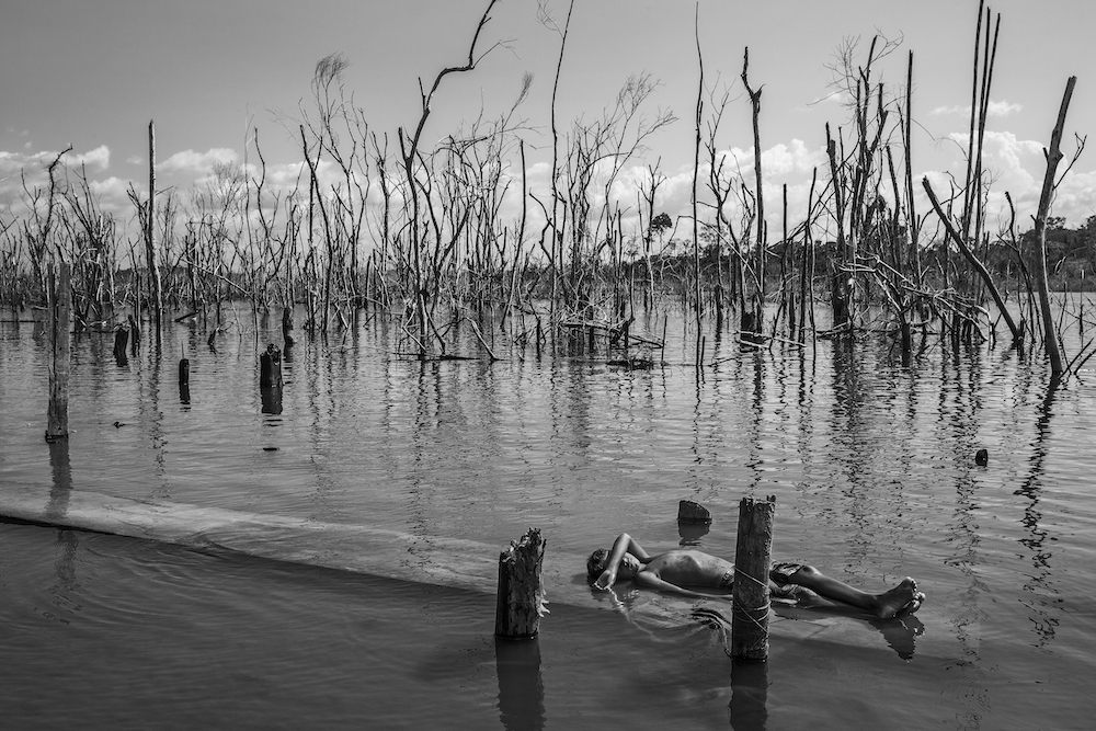 A boy rests on a dead tree trunk in the Xingu River in Paratizão, a community located near the Belo Monte hydroelectric dam, Pará, Brazil, on 28 August 2018. He is surrounded by patches of dead trees, formed after the flooding of the reservoir