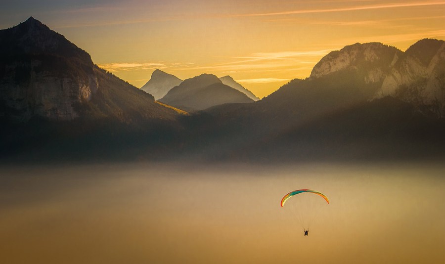 Rainbow parachuter above the clouds in the mountains