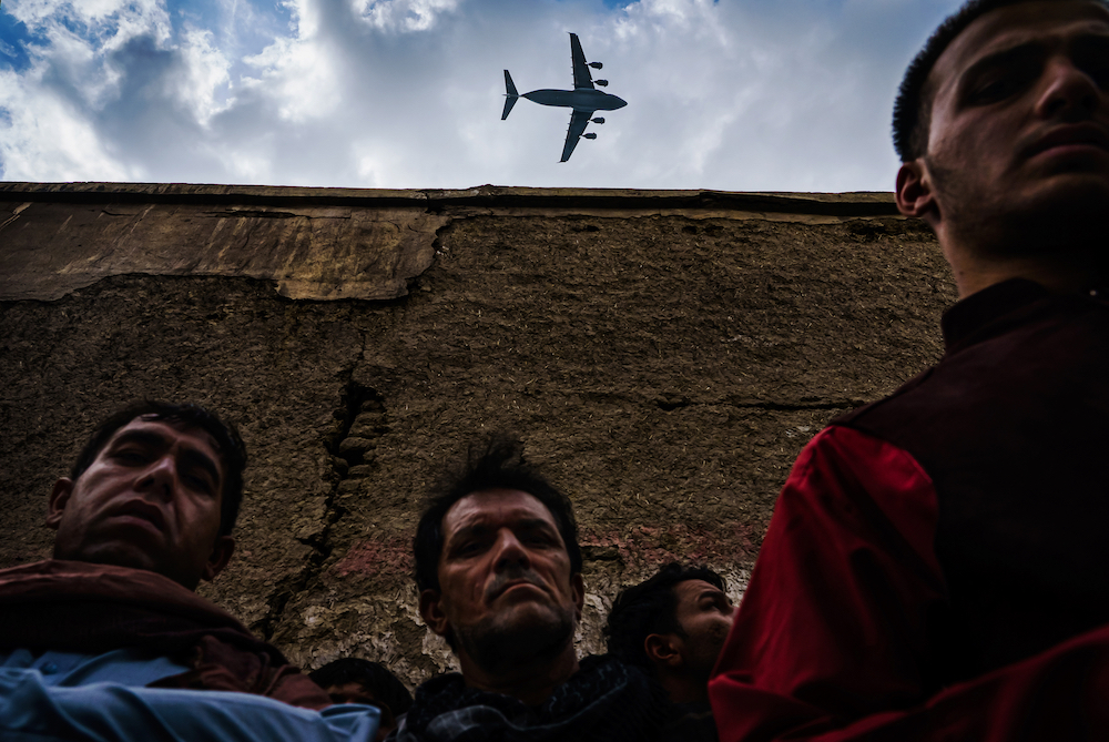 A military transport plane flies over relatives and neighbours of the Ahmadi family as they gather around an incinerated husk of a vehicle destroyed by a US drone strike in Kabul, Afghanistan. In August, life came to a standstill as the Taliban offensive reached the gates of the Afghan capital, sending it into a panic. President Ashraf Ghani escaped; American-backed Afghan forces pulled back. The Taliban swiftly took over a nation that had changed much since it first ruled two decades ago. Jarring, violent scenes followed, marking a tragic coda to a messy and controversial 20-year occupation. The US was ending its longest war. © Marcus Yam/Los Angeles Times