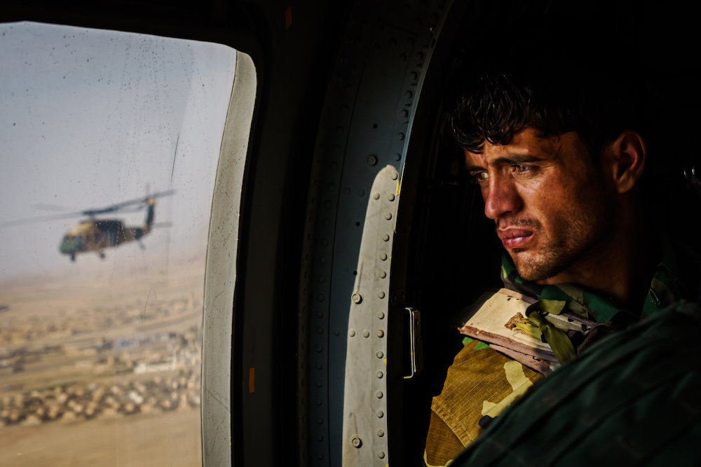 A soldier surveys the terrain out of the window of a UH-60 Black Hawk during a resupply flight toward an outpost in the Shah Wali Kot district north of Kandahar, Afghanistan, on 6 May 2021. The Afghan Air Force, which the US and its partners have nurtured to the tune of $8.5 billion since 2010, is now the government’s safeguard in its fight against the enemy. Since May 1, the original deadline for the U.S. withdrawal, the Taliban have overpowered government troops, wrestling away control of territories and further denying Afghan security forces the use of roads. As a result, all logistical support to thousands of outposts and checkpoints — including re-supplies of ammunition and food, medical evacuations or personnel rotation — must be done by air.⁣ © Marcus Yam