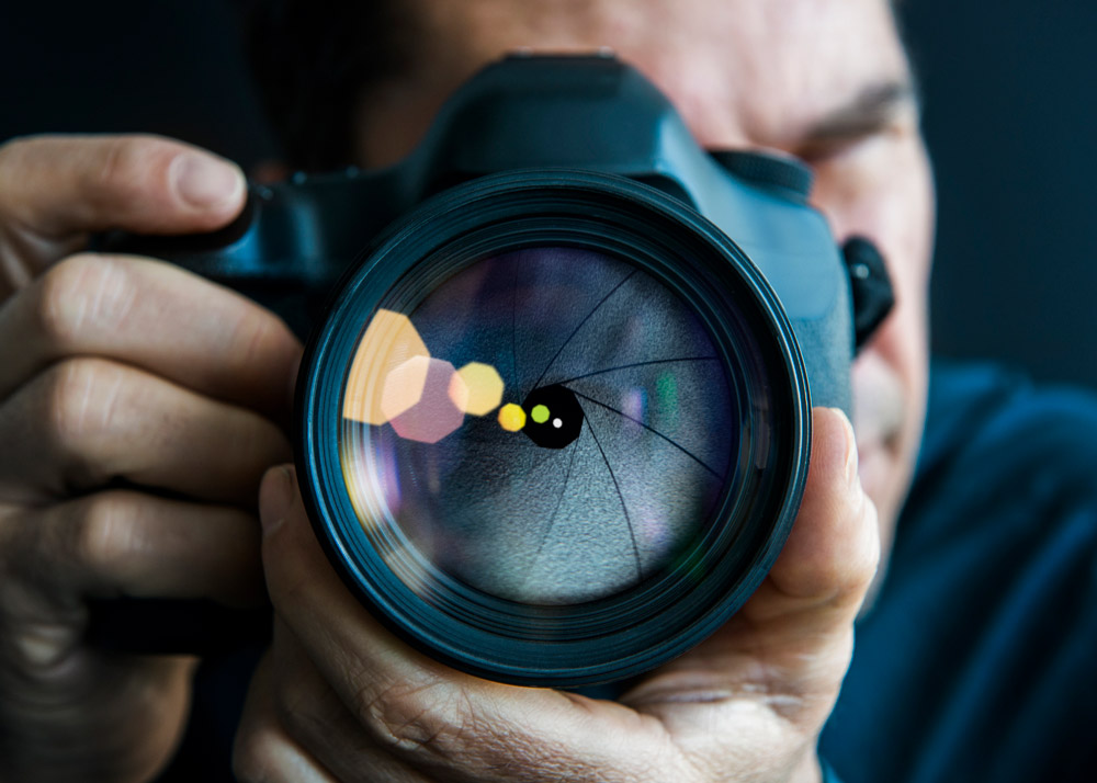 Man holding camera, close-up of lens, showing aperture blades. Credit: Dimitri Otis, Getty Images