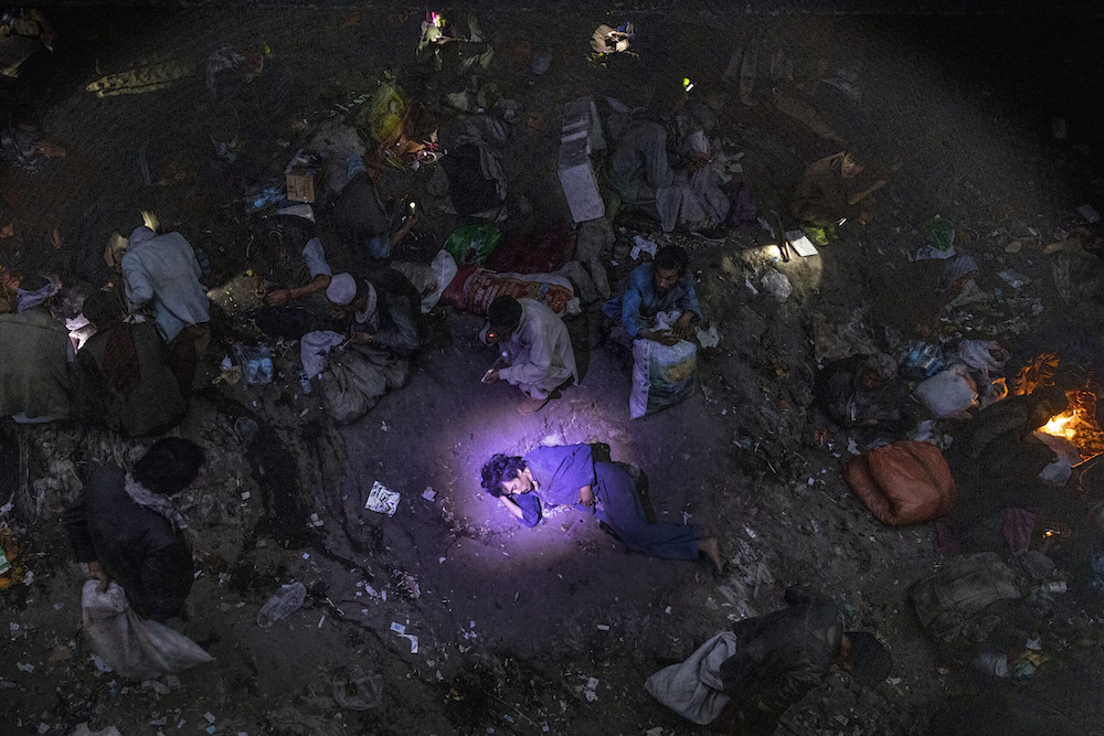 A policeman shines a flashlight on a man suspected of overdosing as drug addicts are seen smoking heroin and methamphetamine in an area where hundreds of users shelter live in squalid conditions at Pul-e-Sukhta, under a bridge in western Kabul © Paula Bronstein, courtesy IWMF