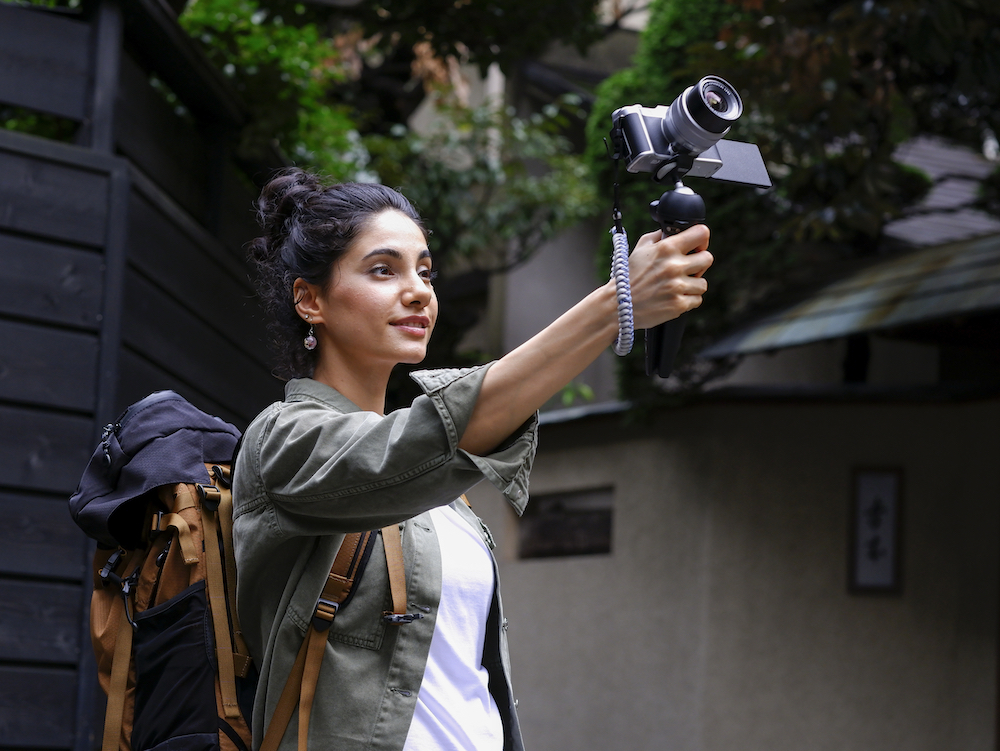 a woman outdoor holding up a small camera on a manfrotto mini tripod vlogging