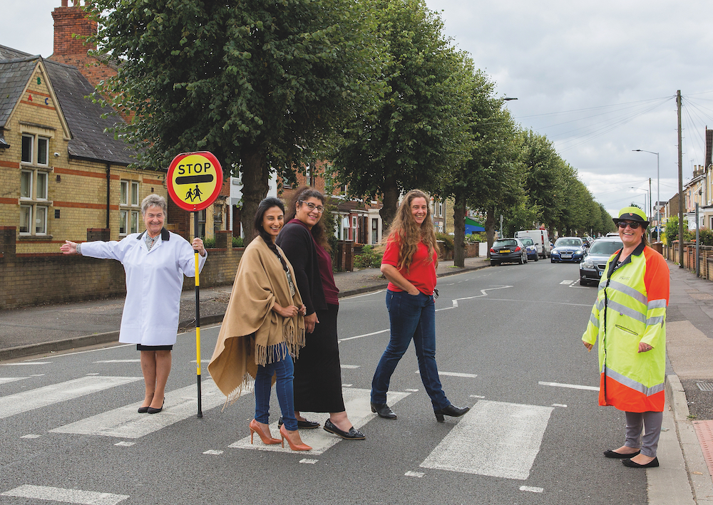 Former lollipop lady Gloria Steele (wearing Tracy Hutchings's, far right, uniform) sees (from left to right) Mazia Ahmad, Gulfraz Umar (nee Malik) and Tanya Porter across the road at Queen's Drive School, Peterborough, September 2020. © Chris Porsz