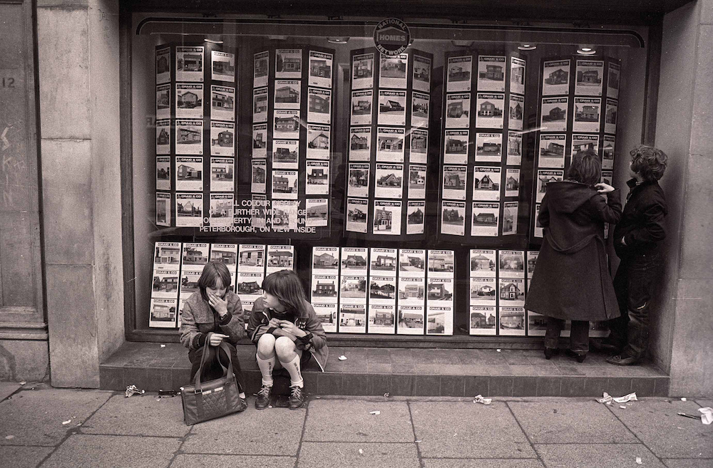 Friends Angela Baxendell (nee Leask, left) and Beverley Barkley (nee Knight, right) waiting to catch a bus outside Craig's Estate Agents in Broadway, Peterborough, 1981. © Chris Porsz