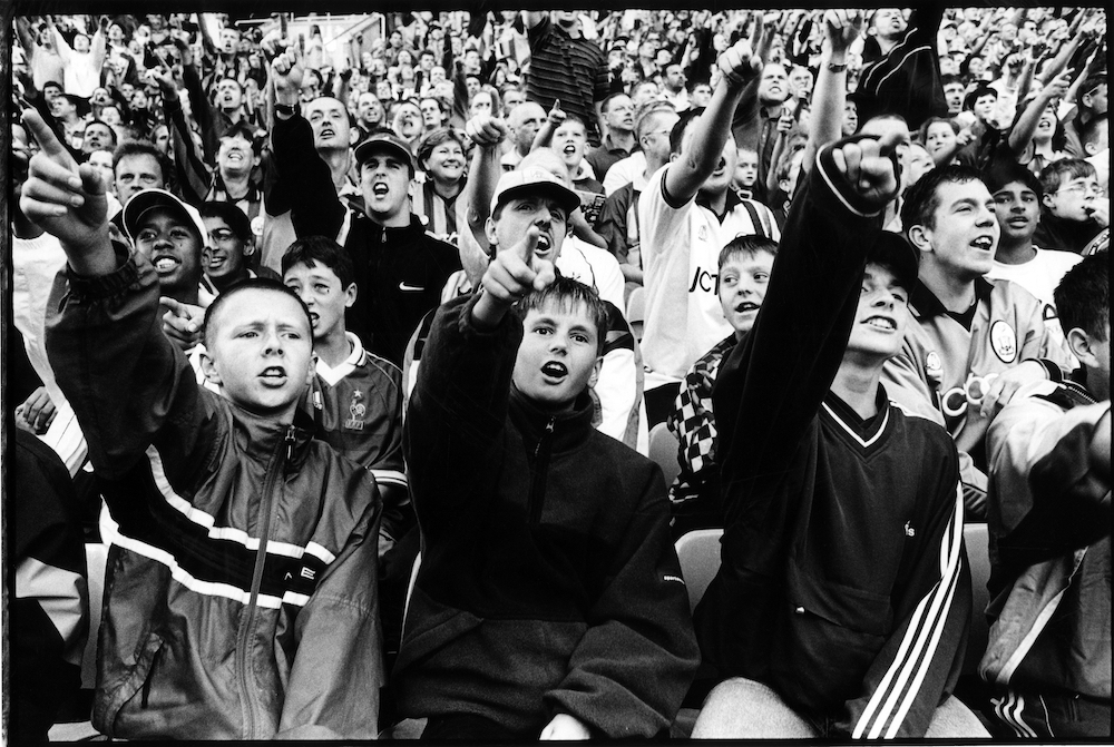 'You're not singing anymore', Bradford City fans in the kop taunt Spurs fans after City equalise in the last minute of the game, 15 September 1999. Ian Beesley explained, 'On 9 May 1999, Bradford City was promoted to the Premier League. In July I was appointed the artist in residence for the 1999-2000 season. I found the transition from ardent fan to photographer, from spectator to observer, very difficult indeed. I confess I missed quite a lot of photo opportunities by becoming far too involved in the game, but, hey, so what - I’m a Bantams fan first, a photographer second!' © Ian Beesley